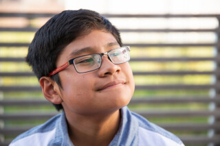 Kid with glasses looking away from camera and smiling